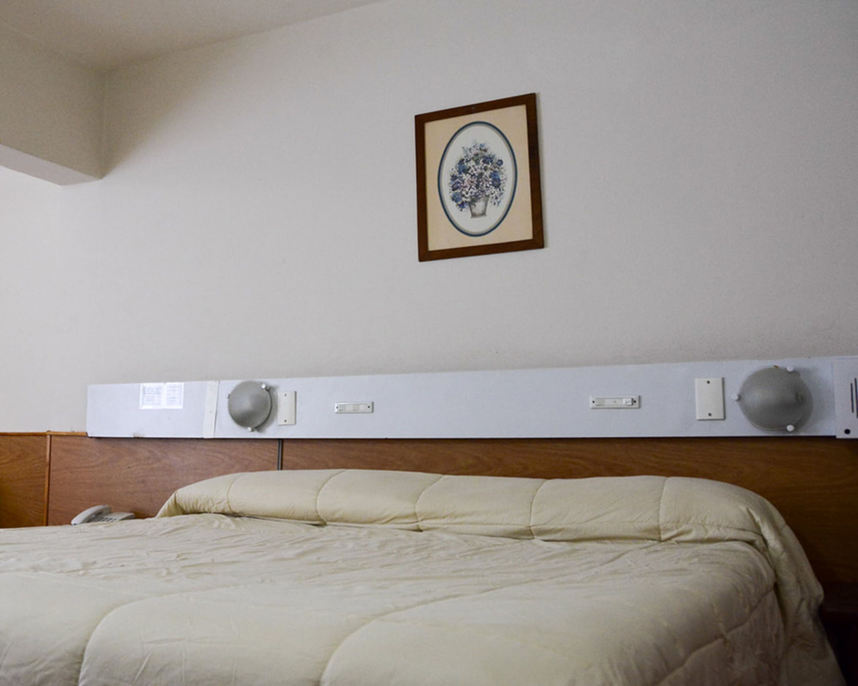 A hotel room with a bed, a headboard with a built-in air conditioning unit, and a framed picture on the wall.
