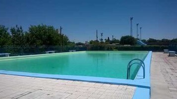 Una piscina con superficie de agua azul cristalina, rodeada por una zona de solárium con baldosas.