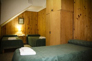 A room with two beds, wooden walls, a framed picture on the wall, and a bedside table with a lamp. - Hotel Menossi (Rio Cuarto)