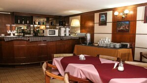 A restaurant with wooden paneling, a bar area with bottles and a microwave, and tables with pink tablecloths. - Hotel Menossi (Rio Cuarto)