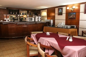 Un restaurante con paneles de madera, una zona de bar con botellas y un microondas, y mesas con manteles rosas.
