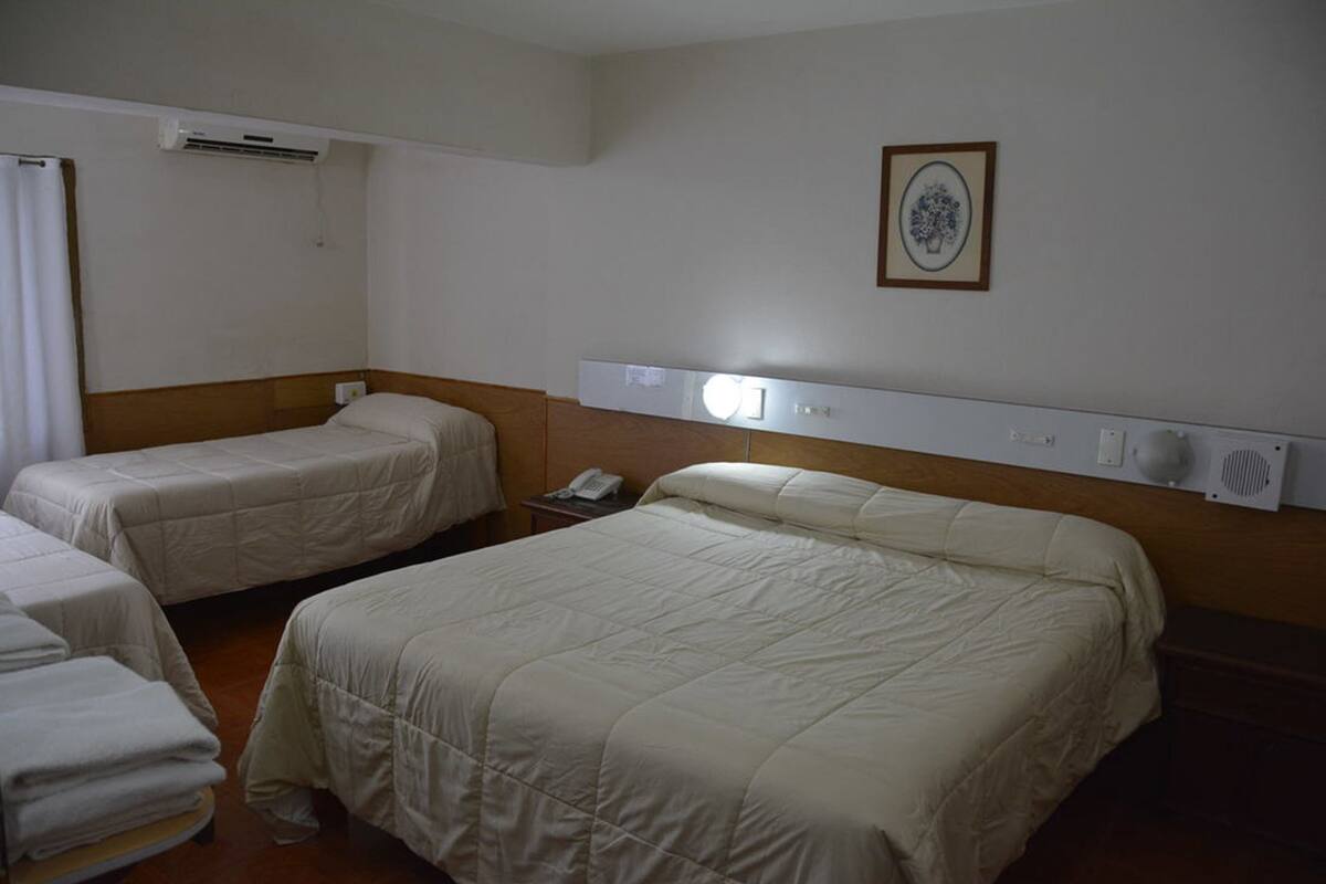 Habitación de hotel con dos camas, una mesita de noche con teléfono, un equipo de aire acondicionado y un cuadro en la pared.