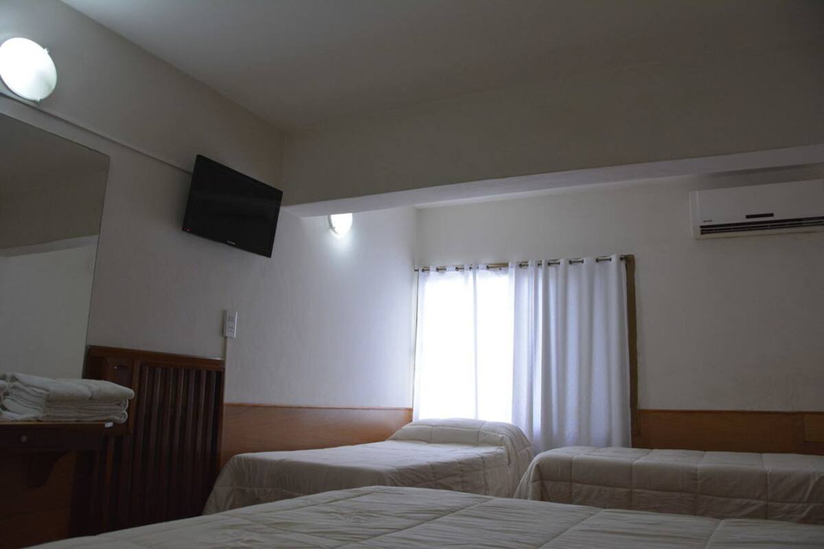 Habitación de hotel con dos camas, un televisor de pantalla plana montado en la pared, una ventana con cortinas y un equipo de aire acondicionado.