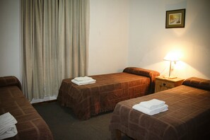 A hotel room with two single beds, a nightstand with a lamp, a window with curtains, and a framed picture on the wall. - Hotel Menossi (Rio Cuarto)