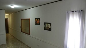 A hallway with a large mirror, two framed pictures, and a window with white curtains. - Hotel Menossi (Rio Cuarto)