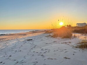 A beach with footprints and tall grass in the foreground, a house in the background, and the sun setting over the ocean. - “Going Coastal”- Newly Remodeled 1950's Beach Cottage (Edisto Island)