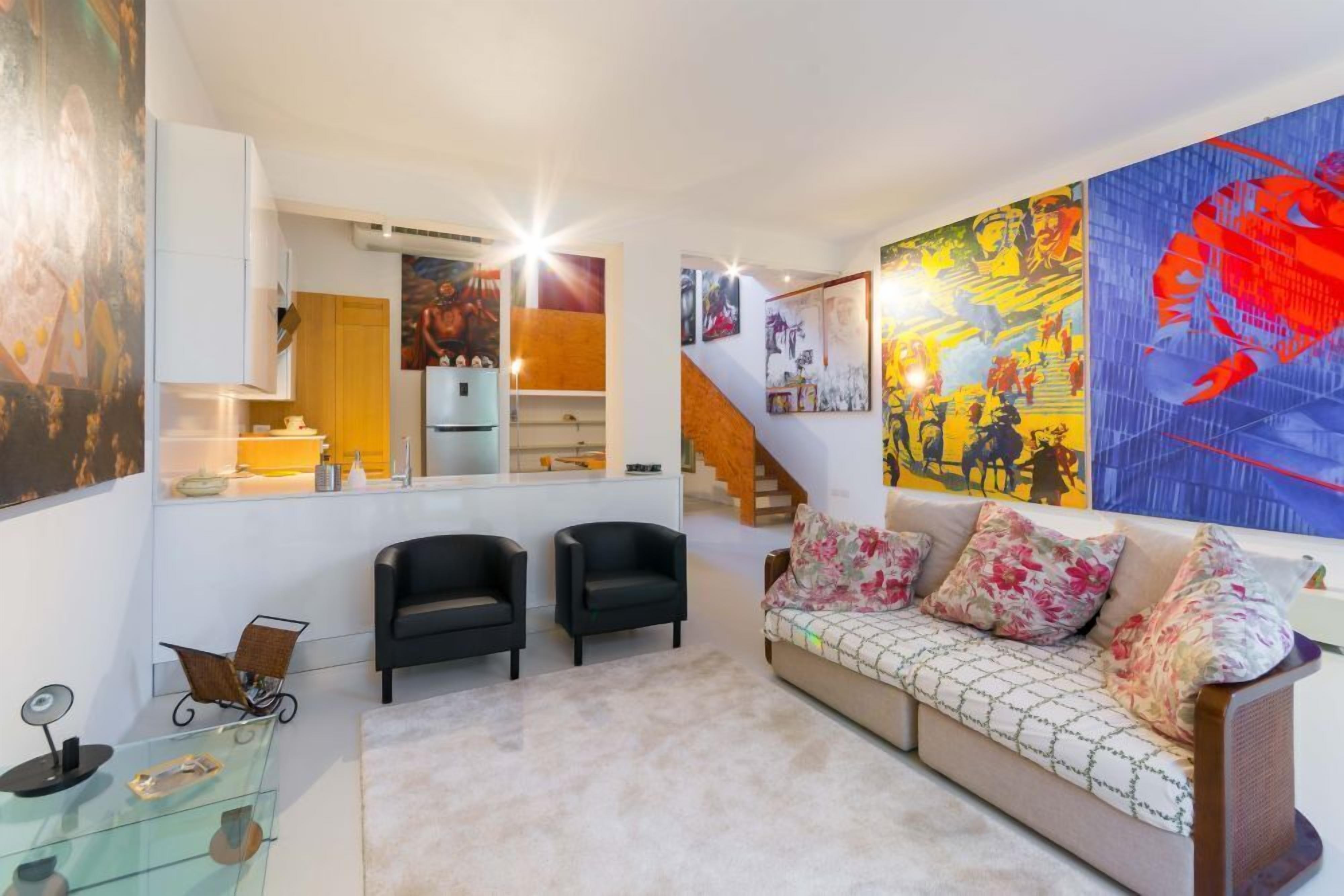 A modern living room with a sofa, two armchairs, a glass coffee table, and a large abstract painting on the wall.