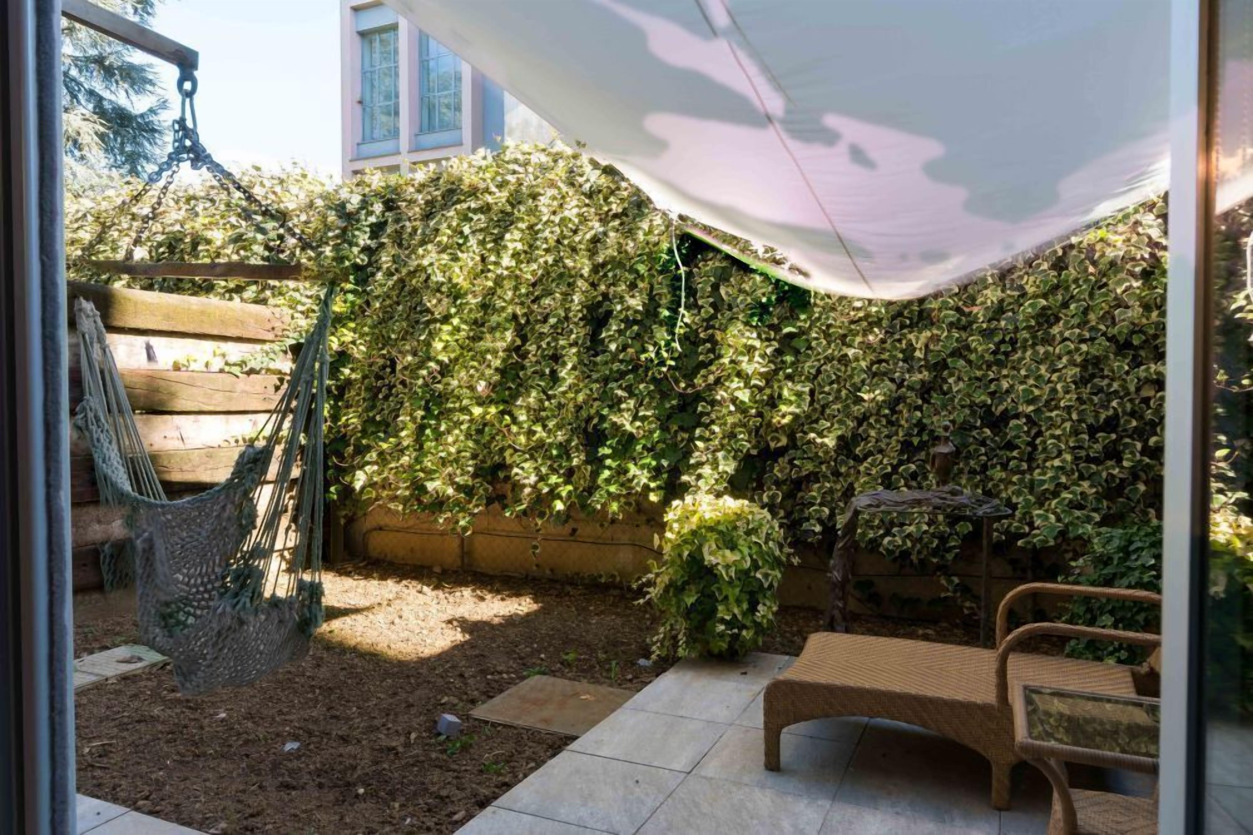 Un patio con una hamaca, un banco y una zona con sombra.