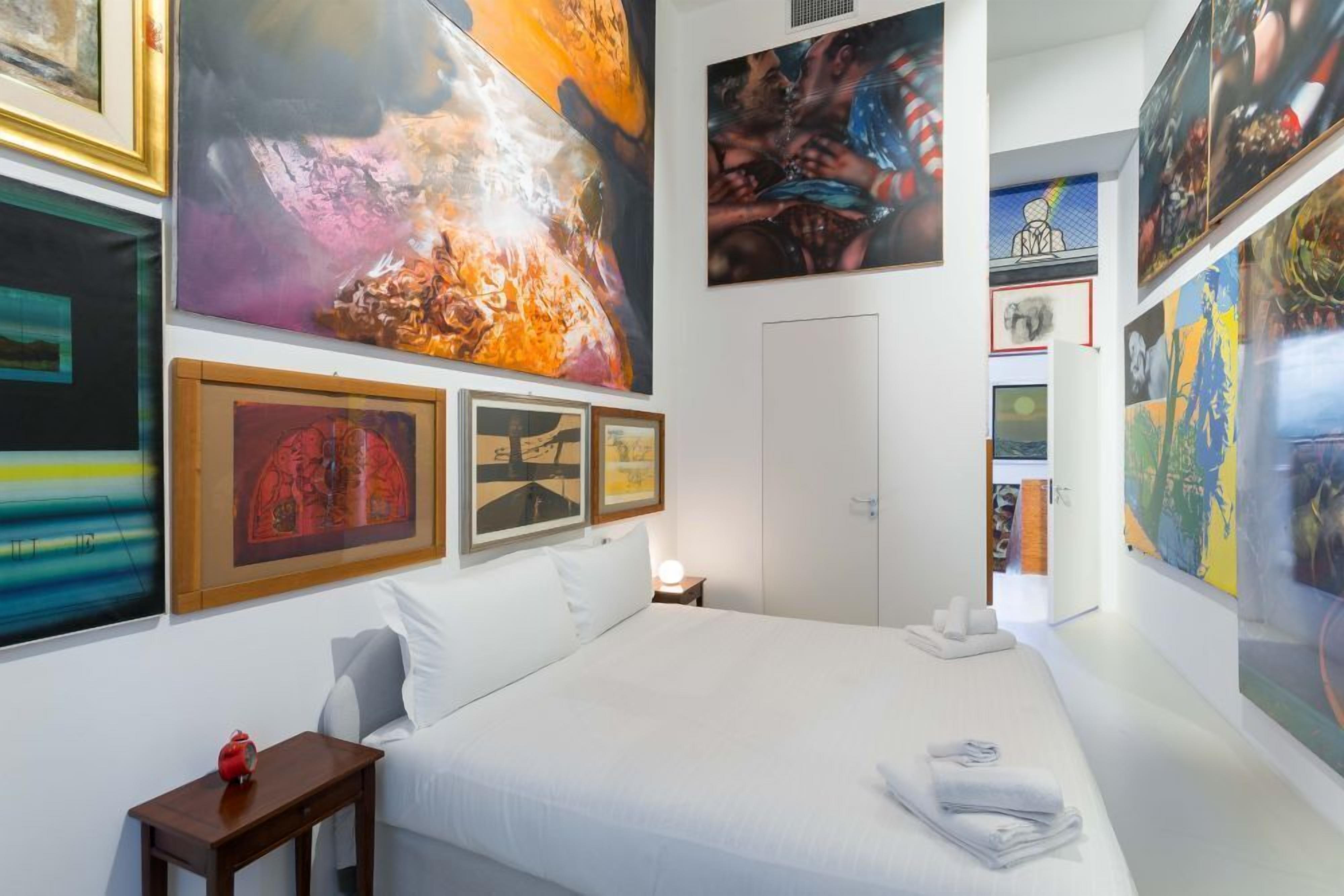 A hotel room with a large bed, a bedside table, and artwork on the walls.