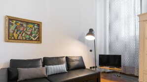 A modern living room with a black leather sofa, a flat-screen TV, a floor lamp, and a painting on the wall. - Naviglio 89 Apartment (Milan)