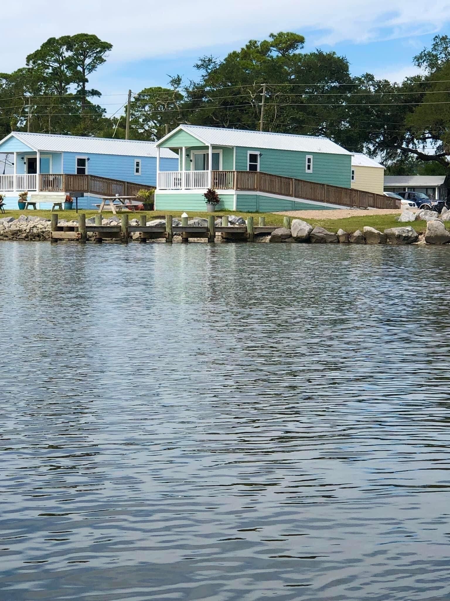 Two waterfront cabins with wooden decks and a dock extending into the water.