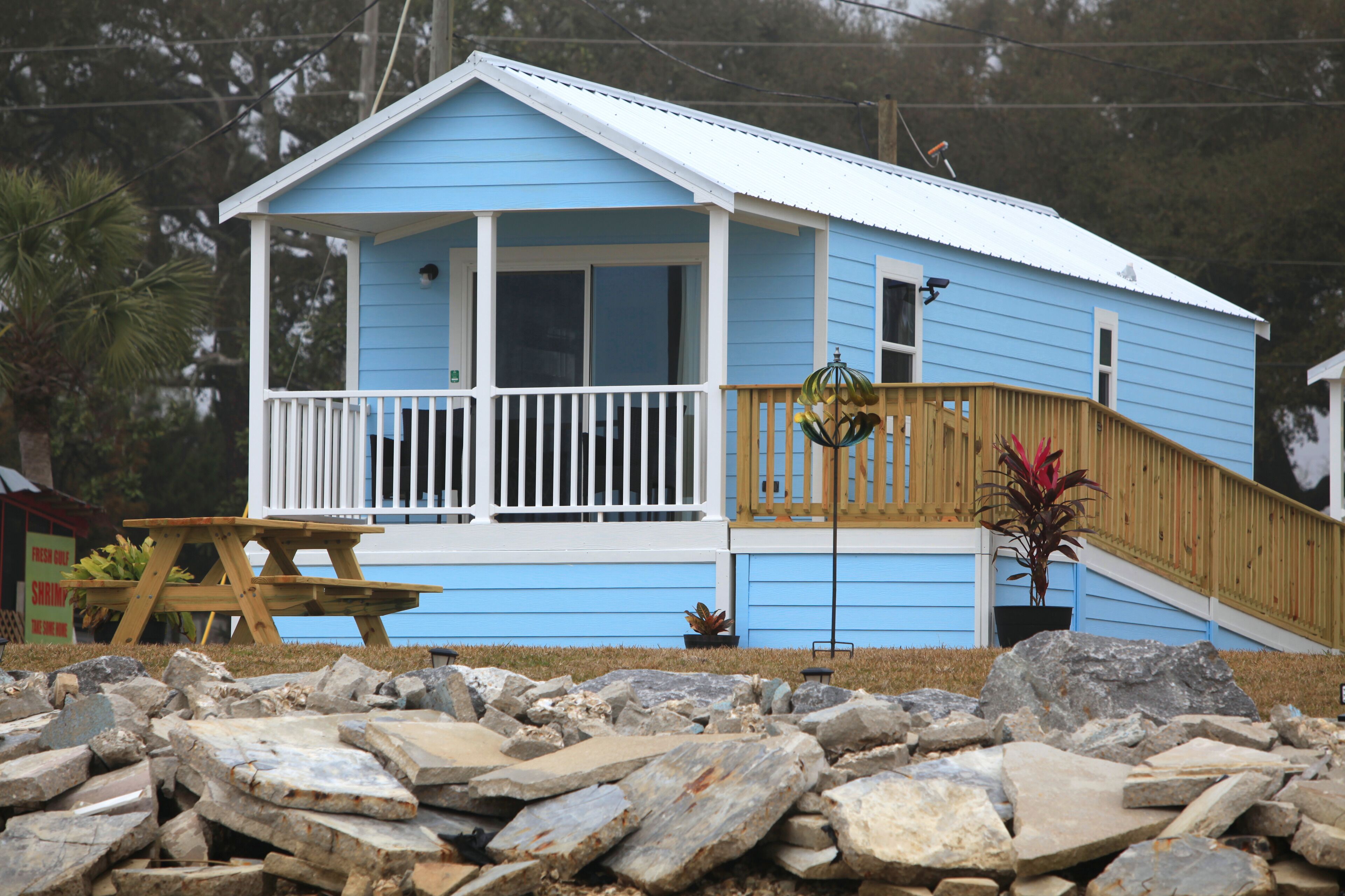 A blue house with a porch, a wooden staircase, and a picnic table.