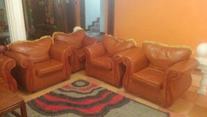 Una sala de estar con tres sofás de cuero marrón dispuestos en forma de L, un tapete estampado y una escalera al fondo.