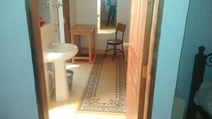 Un pasillo estrecho con un lavamanos, una silla y un espejo en la pared.
