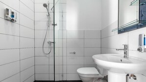 A modern bathroom with white tiles, a glass shower enclosure, a white toilet, and a white sink with a mirror above it. - Studio Apartment on top of old Tbilisi with a 180 degree View of the city (Dzveli Tbilisi)