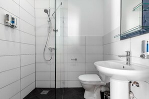 Une salle de bain moderne avec des carreaux blancs, une douche en verre, des toilettes blanches et un lavabo blanc avec un miroir au-dessus.