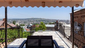 A balcony with a view of a cityscape, a covered area with a patterned floor, and a metal railing. - Studio Apartment on top of old Tbilisi with a 180 degree View of the city (Dzveli Tbilisi)