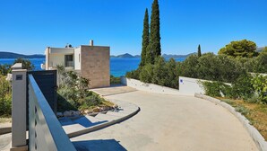A modern building with a view of the sea, a curved driveway, and a tall cypress tree. - Hedera Estate, Villa Hedera XV (Slano)