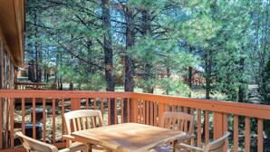 An outdoor deck with a wooden table and chairs, surrounded by trees. - Luxurious Mountain View Golf Resort with tons of Amenities (Flagstaff)
