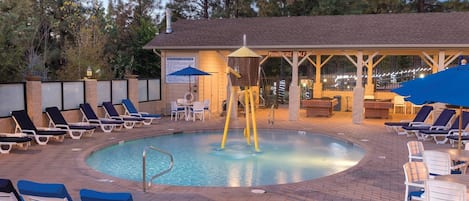 A pool area with lounge chairs, a hot tub, and a covered seating area.