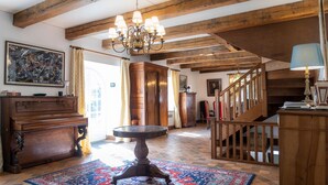A spacious room with exposed wooden beams, a chandelier, a large rug, and a staircase. - Manoir historique • domaine & étang • calme absolu (Pluduno)