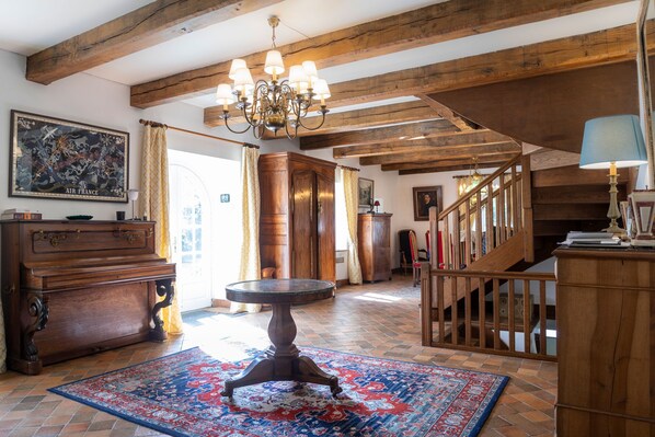 A spacious room with exposed wooden beams, a chandelier, a large rug, and a staircase.