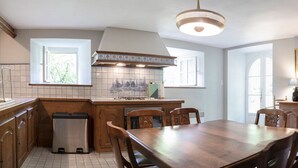 A kitchen with wooden cabinets, a tiled backsplash, a dining table, and chairs. - Manoir historique • domaine & étang • calme absolu (Pluduno)