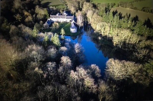 An aerial view of a castle surrounded by dense forest and a small body of water.