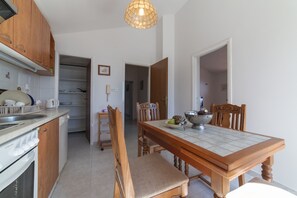 A kitchen with wooden cabinets, a dining table with chairs, and a hanging light fixture. - Apartment Sunrise (Split)