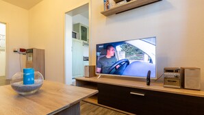 Ein modernes Wohnzimmer mit Fernseher, einer Holzunterhaltungsecke und einer Glasfischkugel auf einem Holztisch.