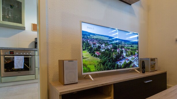 Ein Flachbildfernseher an einer Holzwand, darüber ein Regal.