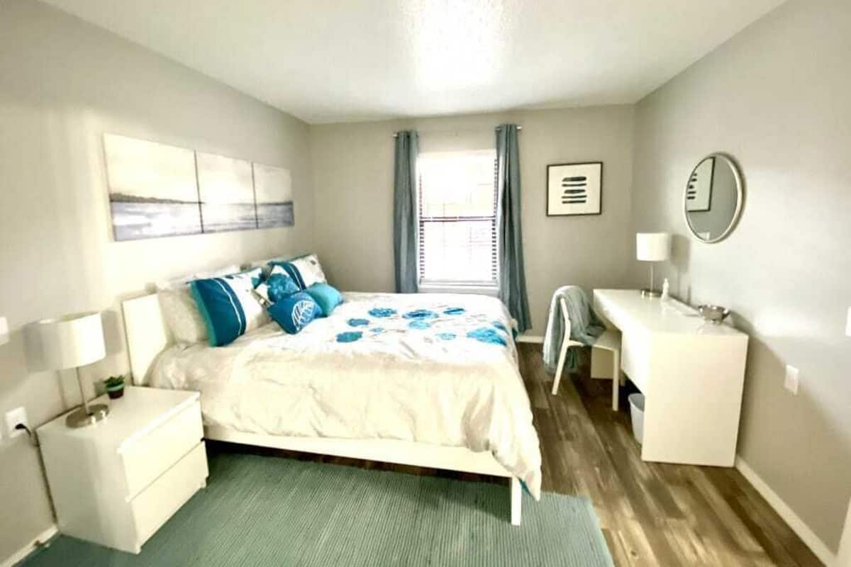 A bedroom with a bed, bedside table, desk, chair, and a window with curtains.