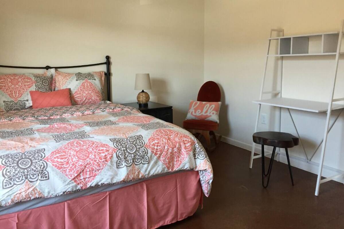 A neatly arranged bedroom with a bed, bedside table, lamp, chair, and a white shelf unit.