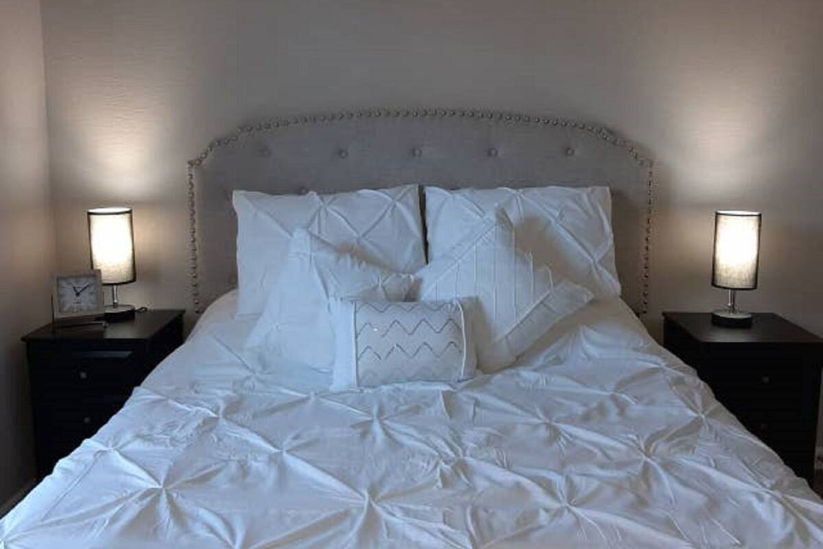 A neatly made bed with a quilted cover, two bedside tables with lamps, and a wall with a subtle pattern.