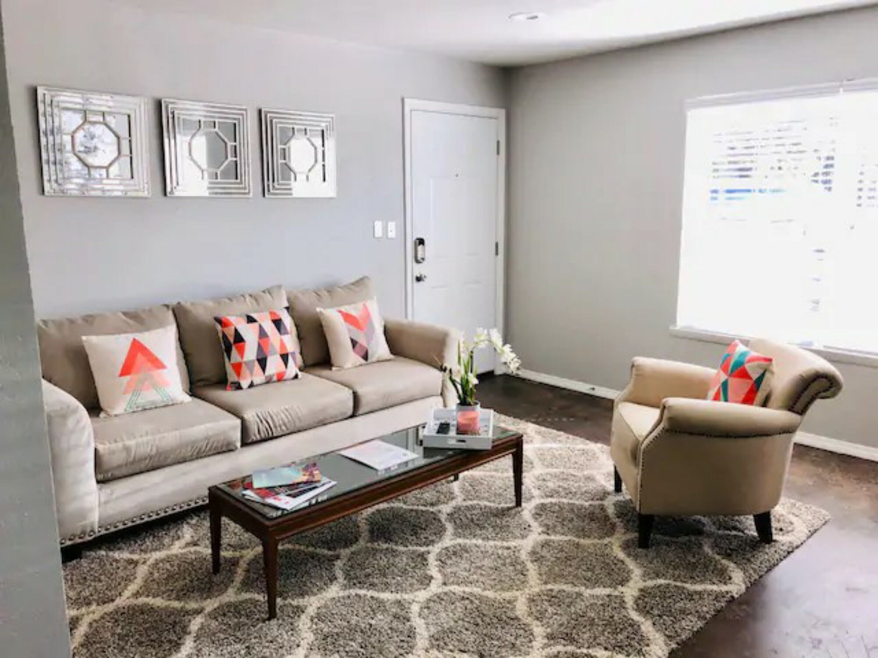 A living room with a beige sofa, a coffee table, and a chair. There are three wall art pieces above the sofa.