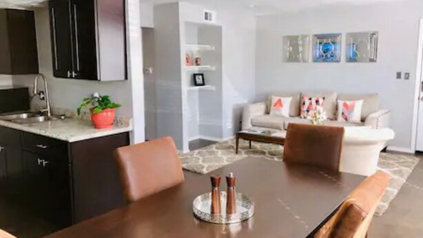 A modern kitchen with dark cabinets, a dining area with a round table, and a living room with a sofa and decorative pillows. - 2 Bedroom Apartment near OU (Norman)