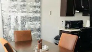 A dining area with a wooden table and four chairs, a coffee machine, and a kitchen area with cabinets and a countertop. - 2 Bedroom Apartment near OU (Norman)