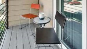 A balcony with a small table and two chairs, a window with a view of buildings, and a wall-mounted light fixture. - Evie's Campus-close 2 bedroom luxury (Norman)