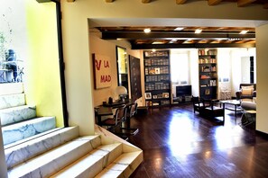 A spacious living area with a marble staircase, a dining area with chairs and a table, and a bookshelf filled with books.