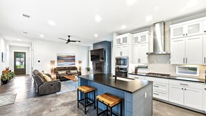 Een moderne keuken met witte kasten, een centraal kookeiland met barkrukken, en een zithoek met een bank en salontafel.