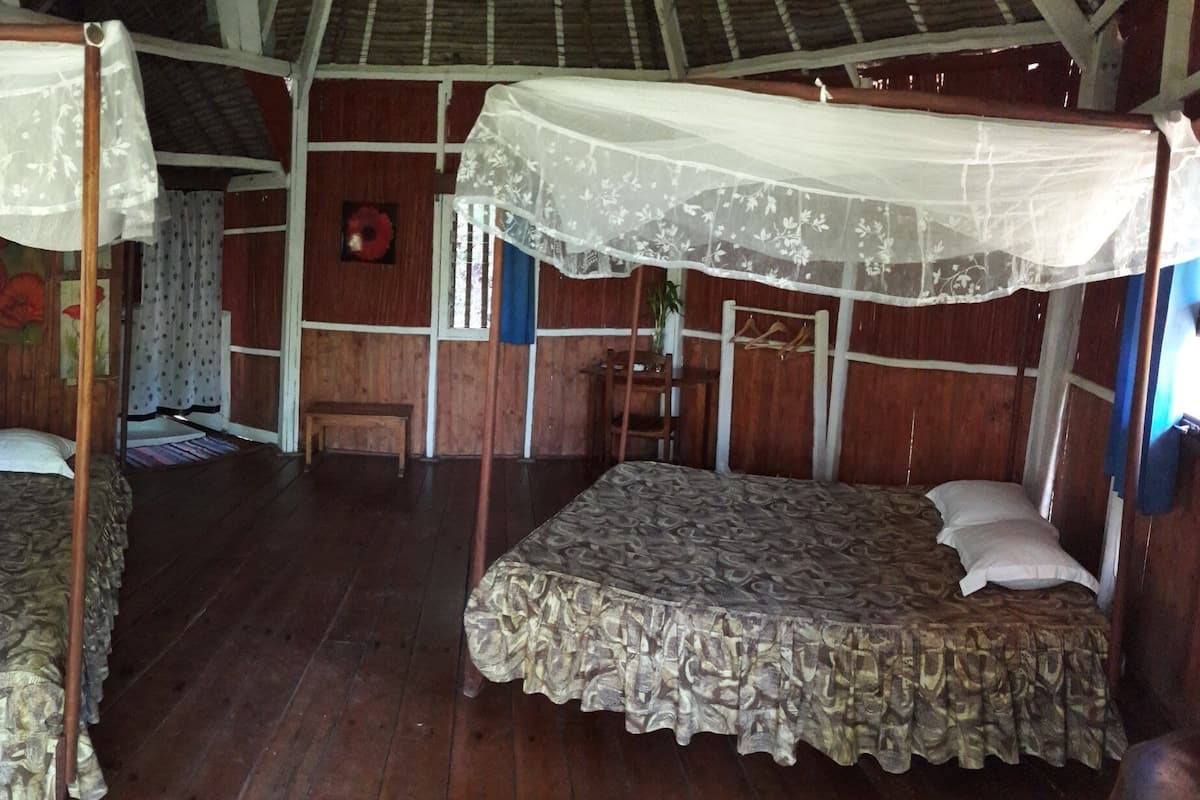 A room with two single beds, each with a canopy, wooden walls, and a bench.