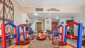 A dining area with a long wooden table, red and blue chairs, and a woven placemat. - Princesa Resort D-509 Whispering Sands Great Ocean View Condo (Puerto Peñasco)