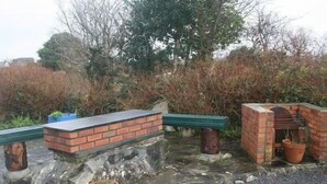 Un banc en pierre avec un rebord en briques, un four en briques et une plante en pot.