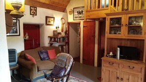 Un salon chaleureux avec un plafond en bois, un canapé, un fauteuil, un meuble avec des portes en verre et un téléviseur.