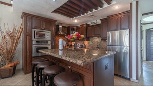 Una cocina con armarios de madera oscura, electrodomésticos de acero inoxidable, encimera de granito y una isla central con taburetes.