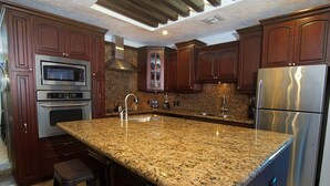 Una cocina con encimeras de granito, electrodomésticos de acero inoxidable, armarios de madera y horno empotrado.