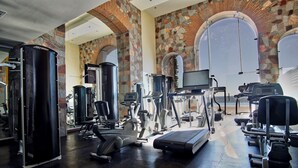 Un gimnasio con diversos equipos de ejercicio, como cintas de correr y máquinas de pesas, bajo techos de piedra abovedados.