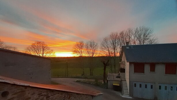 A rural landscape with a sunset, a stone wall, and a building with a grey roof.