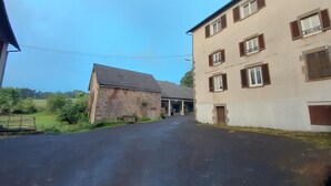 A rural road leading to a stone building with a metal roof and a multi-story building with brown shutters.