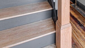 Una escalera de madera con barandilla blanca y una planta a su lado.